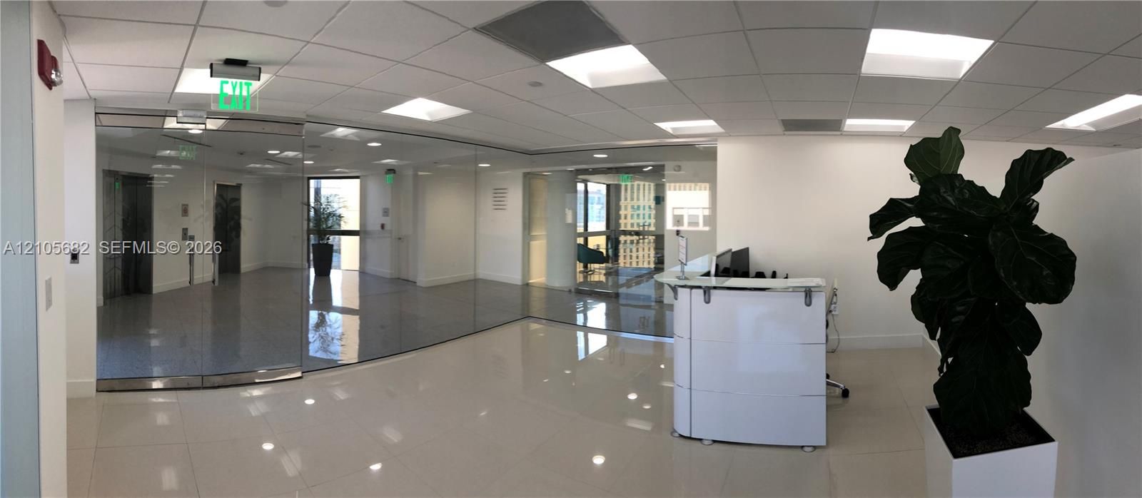 Reception area featuring large-format polished tile flooring, recessed grid ceiling with integrated panel lighting, floor-to-ceiling glass partitions, and a built-in modular reception desk