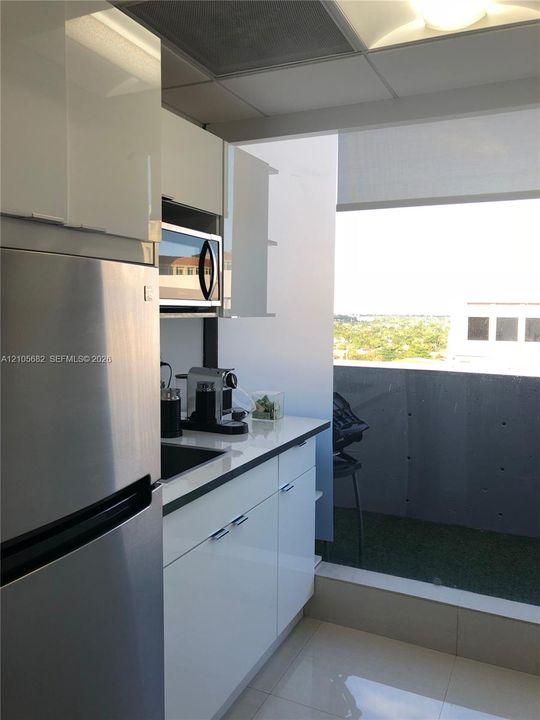 Kitchenette featuring high-gloss white cabinetry, polished countertop, stainless steel refrigerator, built-in microwave, and large-format tile flooring