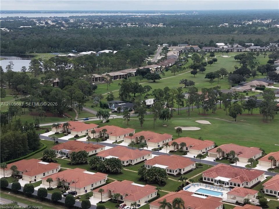 Aerial perspective of a community featuring terracotta-tiled roofs, manicured lawns, mature landscaping, paved roadways, and a communal pool