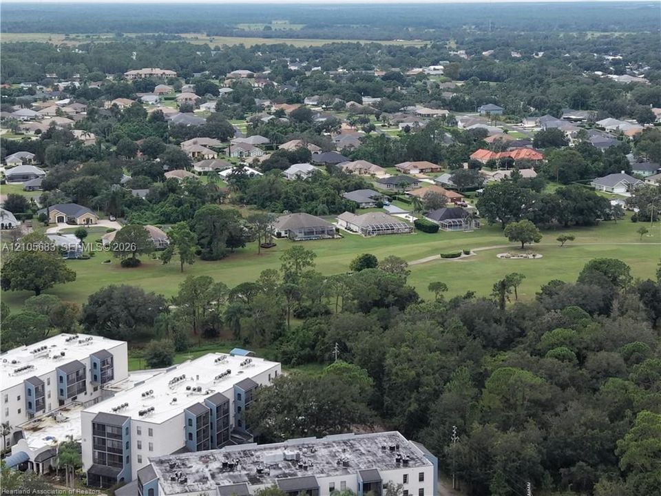 Aerial perspective of a multi-story residential building complex featuring white stucco facades, flat roofing systems, and expansive green space with mature trees