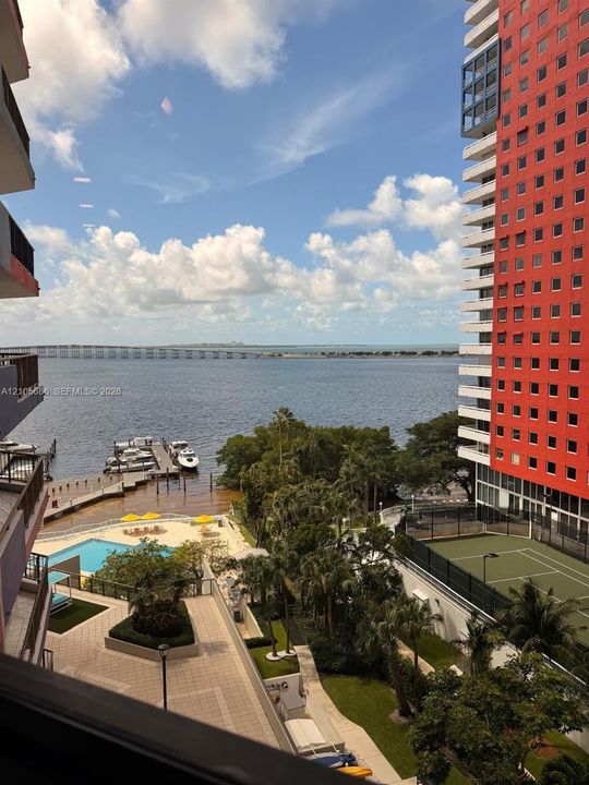 Waterfront setting featuring a private dock, outdoor swimming pool, tennis court, and manicured landscaping