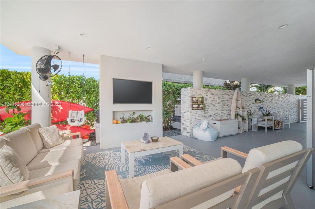 Covered outdoor patio featuring recessed ceiling lighting, a textured stone accent wall, a built-in wall-mounted television, and a recessed display niche