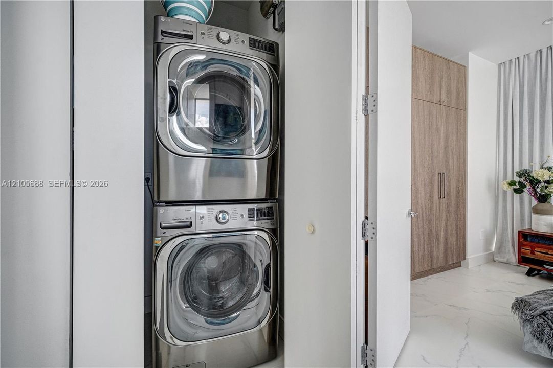 Stackable stainless steel front-load laundry appliances housed in a built-in closet with floor-to-ceiling wood-finish cabinetry