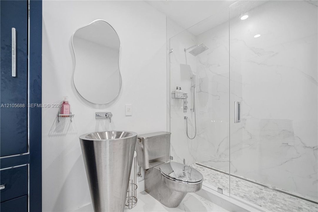 Modern bathroom featuring a metallic pedestal sink with a wall-mounted faucet, frameless glass-enclosed shower with floor-to-ceiling tile, and a contemporary mirror
