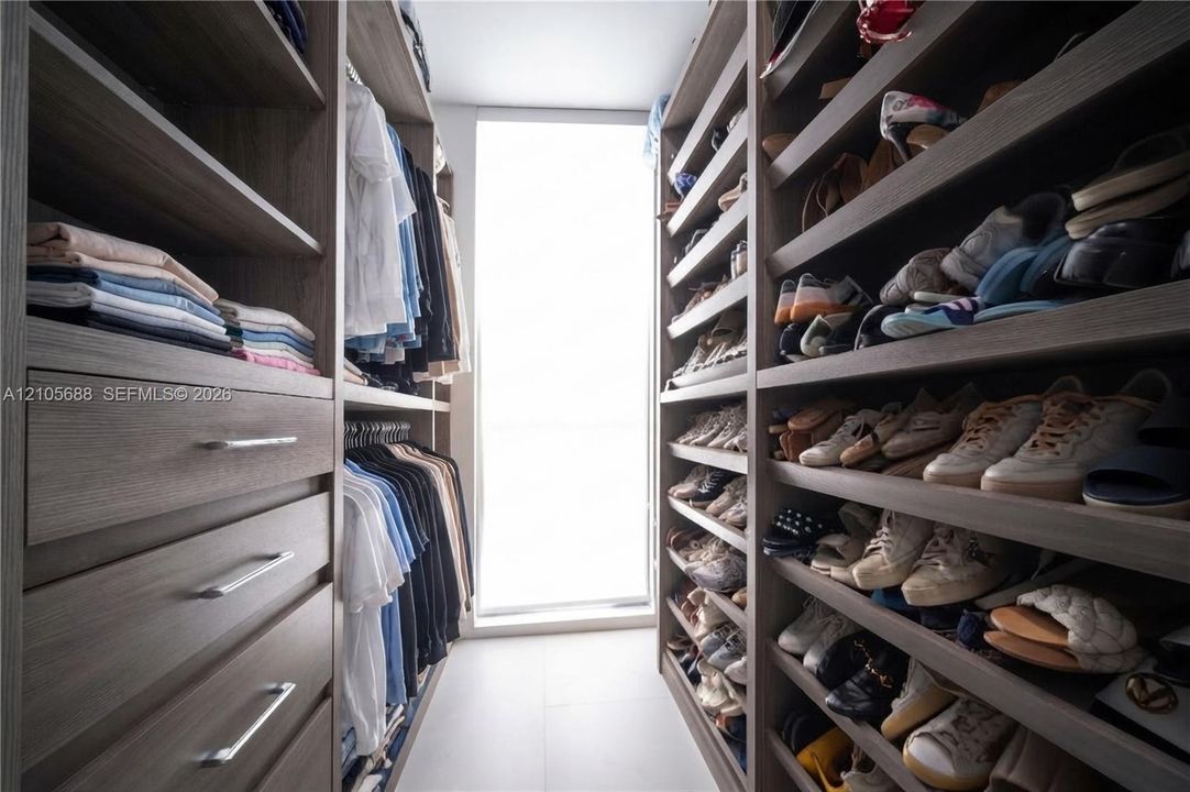 Walk-in closet featuring floor-to-ceiling built-in cabinetry, custom wood-finish shelving, integrated pull-out drawers with metallic hardware, and a full-length window