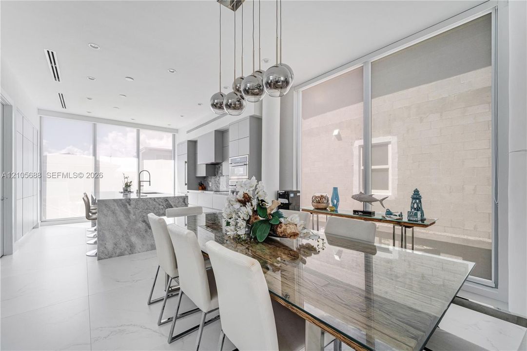 Modern kitchen featuring a waterfall edge stone island, floor-to-ceiling glass panel walls, flat-panel cabinetry, recessed ceiling lighting, and a multi-sphere pendant light fixture