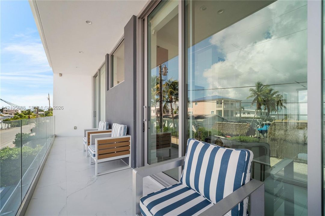 Expansive covered balcony with frameless glass railing, modern sliding glass doors, and polished concrete flooring