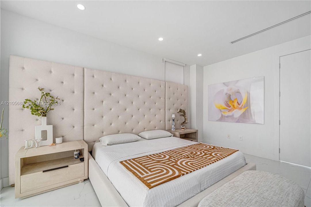 Full-height tufted upholstered headboard, integrated light-toned wooden nightstands, recessed ceiling lighting, and smooth-finish flooring