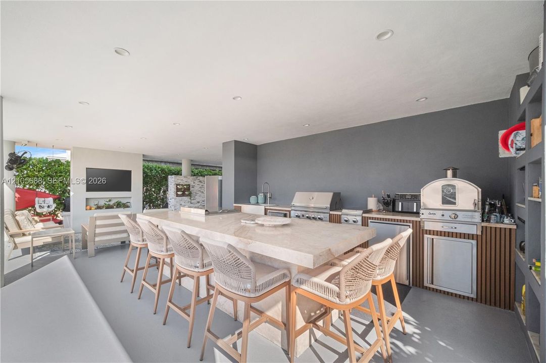 Covered outdoor kitchen featuring a stone-topped island, stainless steel grill, built-in pizza oven, and recessed ceiling lighting