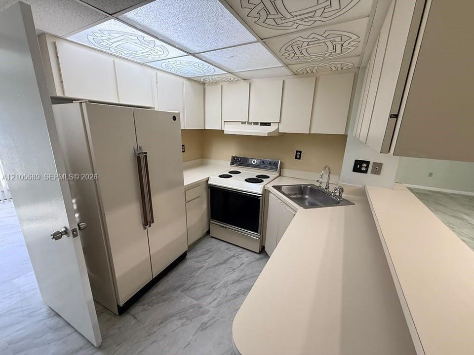 Kitchen featuring neutral cabinetry, solid-surface countertops, a stainless steel sink with a high-arch faucet, an electric range, and patterned drop ceiling tiles