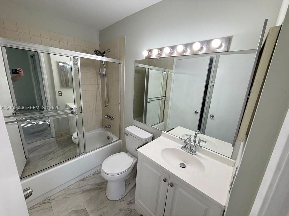 Bathroom featuring a vanity with integrated sink, large wall-to-wall mirror, six-light vanity fixture, and a tub-shower combination with sliding glass doors