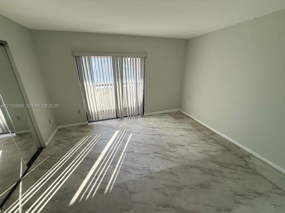 Neutral-toned room featuring large-format stone-patterned tile flooring, floor-to-ceiling mirrored closet doors, and a sliding glass door with vertical blinds
