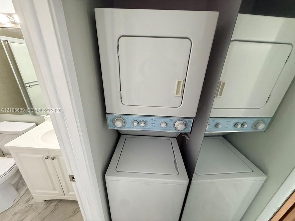 Stacked washer and dryer unit with top-loading machine, white vanity cabinet featuring a recessed sink, and wood-finish flooring