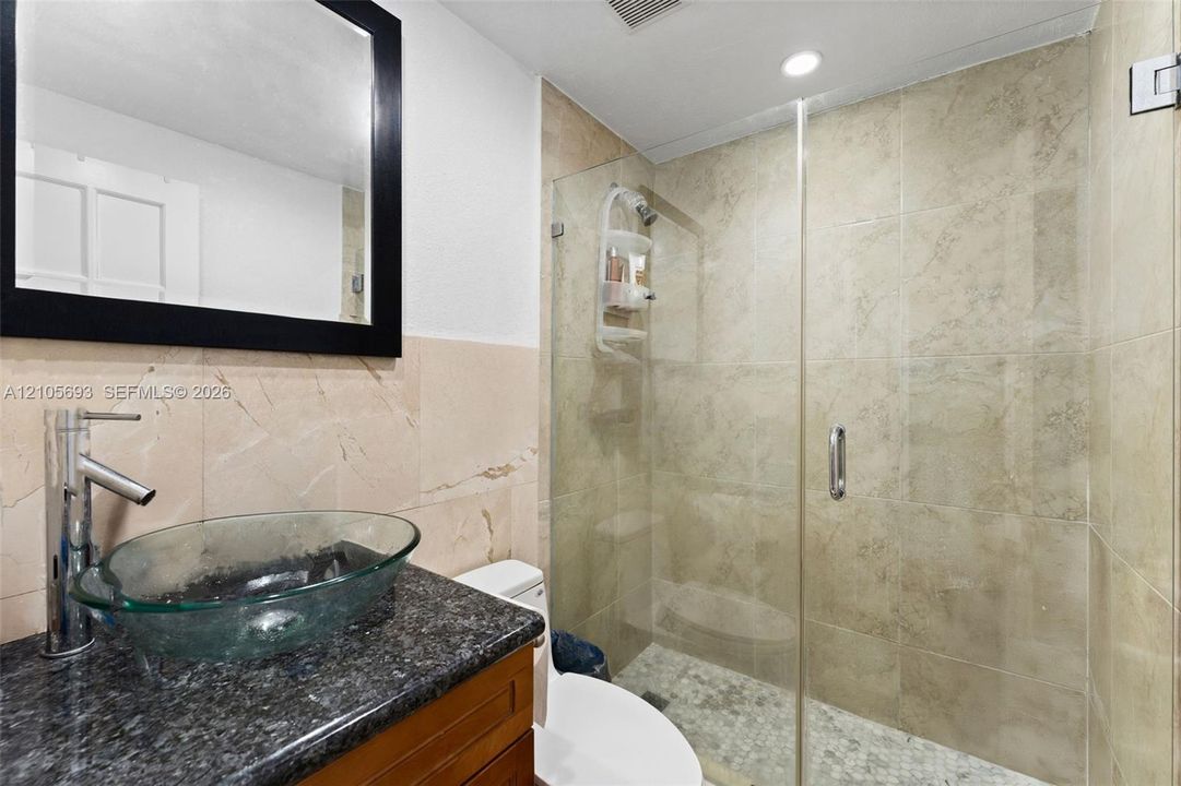 Bathroom featuring a vessel sink with a chrome faucet, stone-finish vanity countertop, large wall-mounted mirror, and a glass-enclosed shower with tiled surround