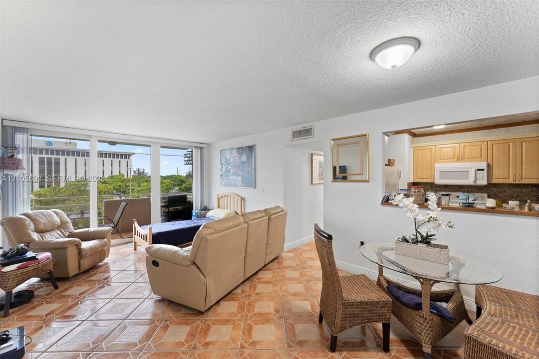 Open living area featuring ceramic tile flooring, floor-to-ceiling sliding glass doors, and a pass-through opening to the kitchen with wood-finish cabinetry