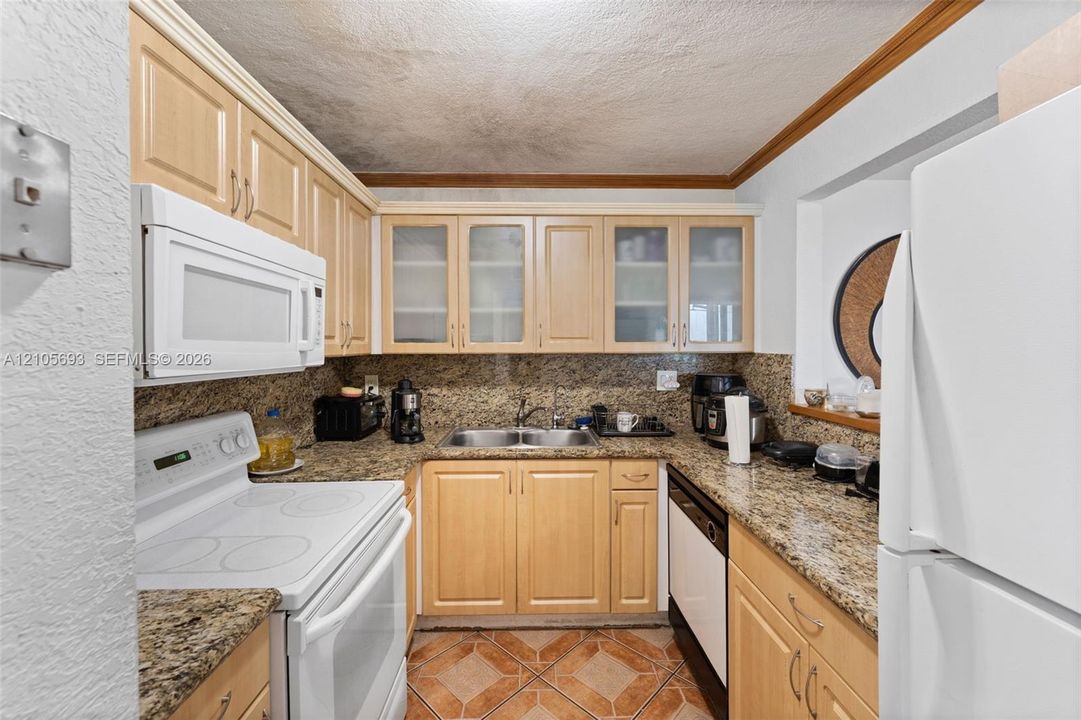 Kitchen featuring wood cabinetry with upper glass-panel inserts, stone-finish countertops, tile flooring, and integrated white appliances