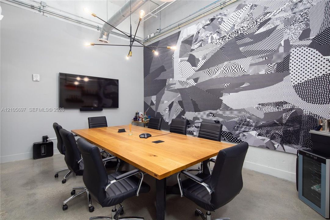 Polished concrete flooring, exposed industrial ceiling ductwork, modern multi-arm chandelier, and accent wall featuring a large-scale graphic pattern
