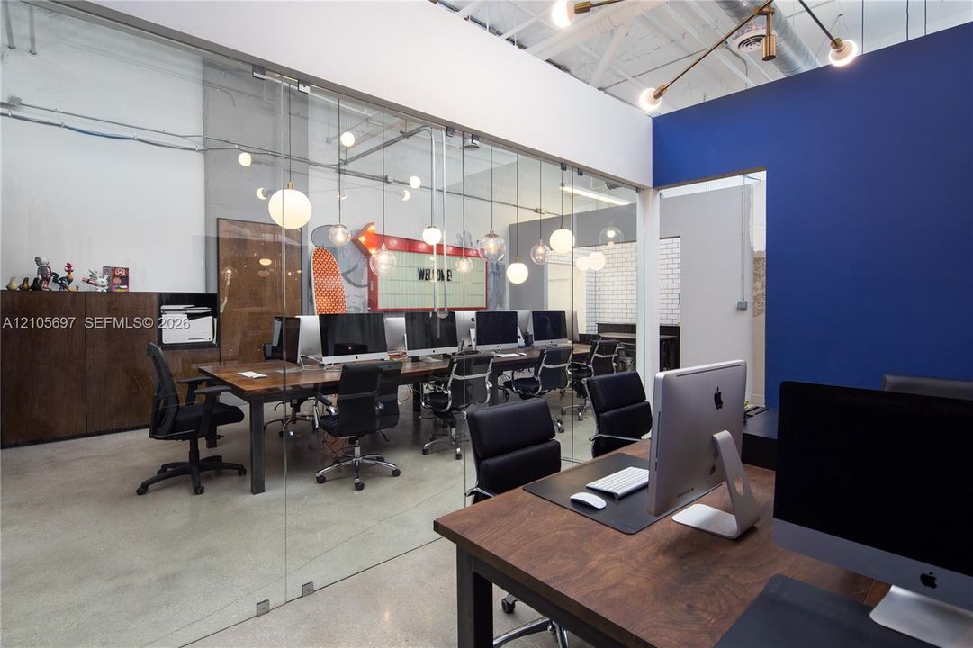 Open-concept workspace featuring polished concrete flooring, floor-to-ceiling glass wall partitions, exposed industrial ceilings, and modern pendant lighting
