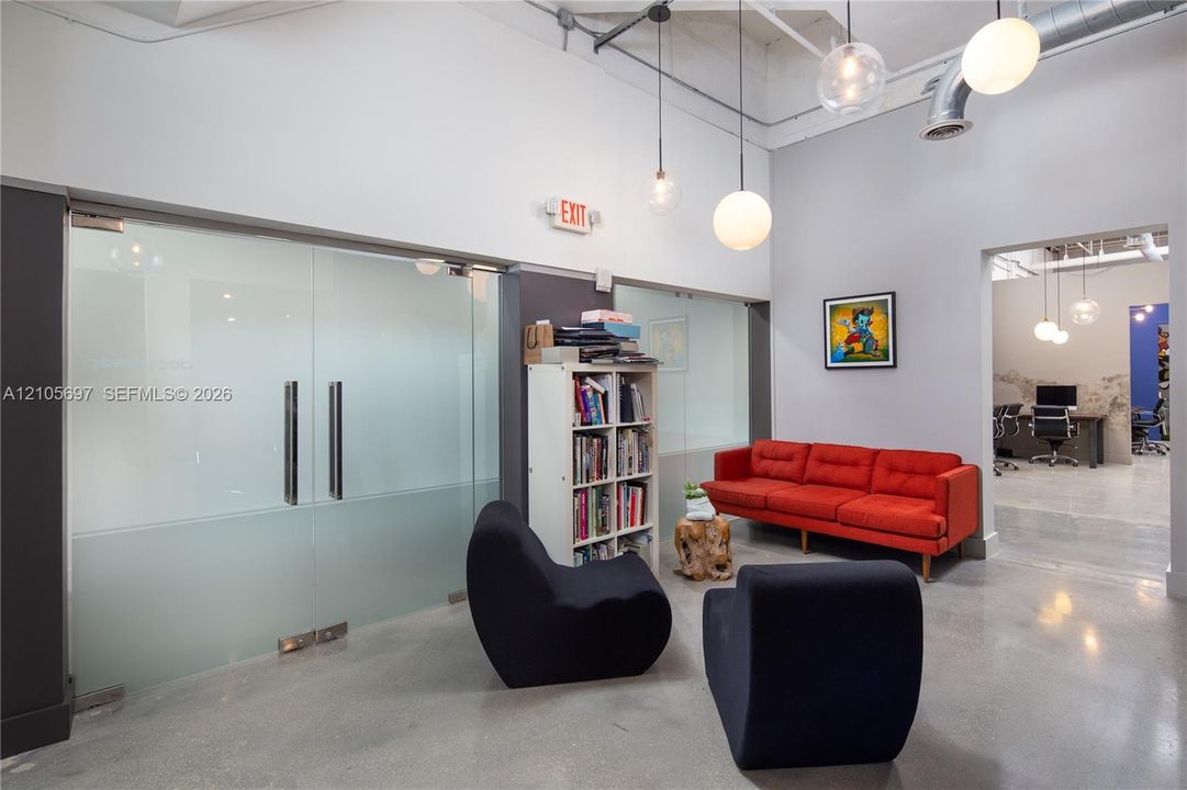 Industrial aesthetic featuring polished concrete flooring, exposed ceiling ductwork, high ceilings, globe pendant lighting, and frosted glass paneled doors with metal hardware