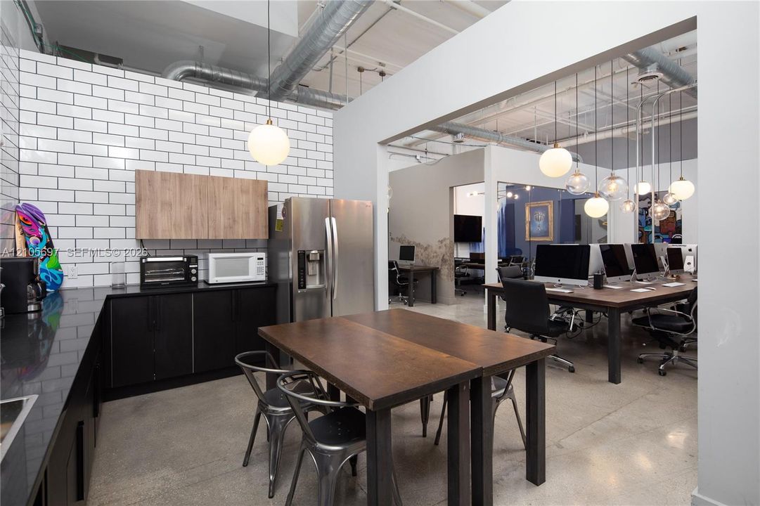 Industrial-style kitchen featuring exposed ductwork, polished concrete flooring, white subway tile backsplash, matte black cabinetry, and globe pendant lighting