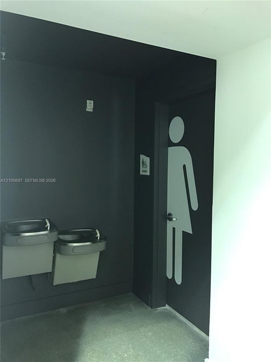 Modern restroom featuring dual wall-mounted waste receptacles, polished concrete flooring, and contemporary signage