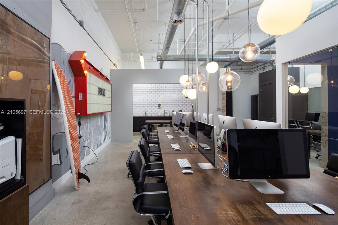 Industrial-style space featuring high ceilings with exposed ductwork, polished concrete flooring, a series of glass globe pendant lights, and a white subway-tile backsplash