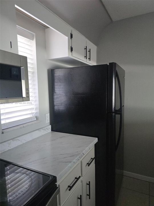 White cabinetry featuring matte black hardware, stone-patterned countertops, and integrated stainless steel and black appliances