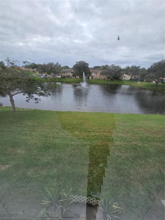 Waterfront lot featuring a pond, a center fountain, and mature trees situated on a grass lawn