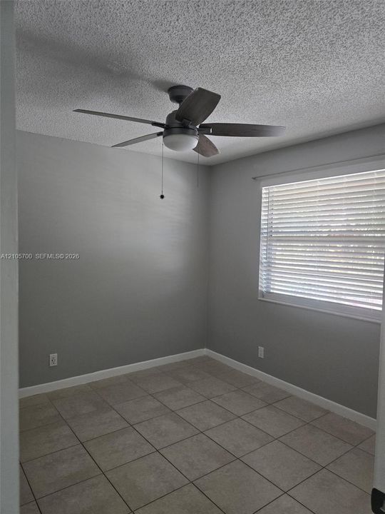 Neutral gray wall paint, ceramic tile flooring, and a ceiling fan with integrated light fixture