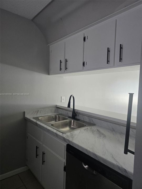 White cabinetry with matte black hardware, stone-finish countertops, stainless steel double-basin sink, and high-arc matte black faucet
