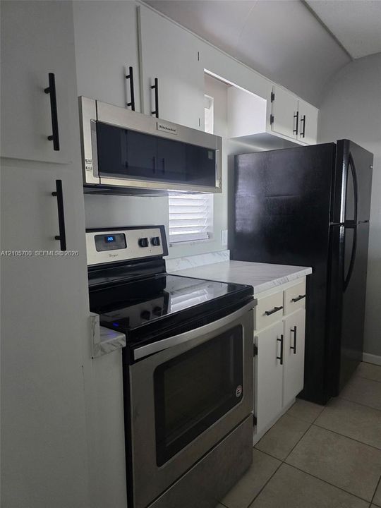 Kitchen featuring white cabinetry with matte black hardware, stone-finish countertops, stainless steel oven and microwave, and large-format tile flooring