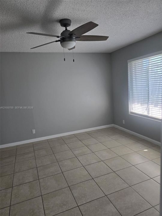 Neutral-toned wall finish, large-format tile flooring, five-blade ceiling fan with integrated lighting, and horizontal window blinds