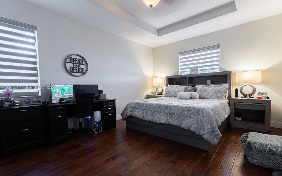 Tray ceiling, wood-finish flooring, and dual windows featuring adjustable roller shades