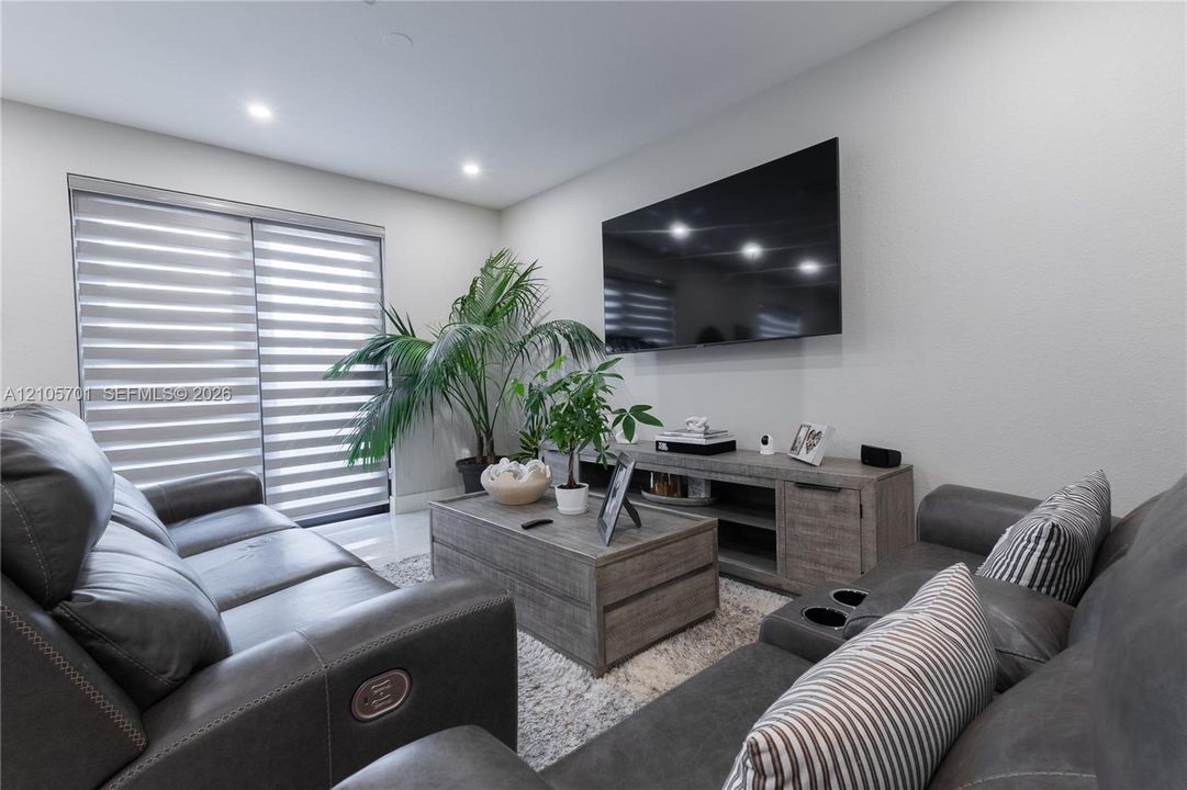 Living space featuring recessed lighting, smooth-finish walls, large-format tile flooring, and sliding glass doors with integrated horizontal window treatments