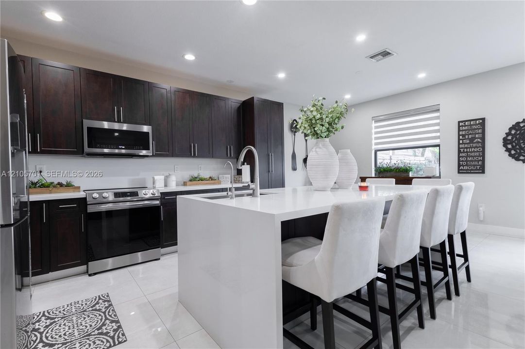 Kitchen featuring dark-finish cabinetry, a central island with a solid-surface countertop, stainless steel appliances, and large-format tile flooring