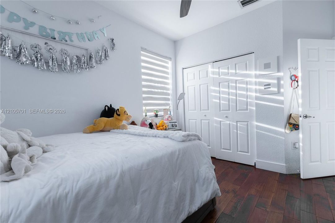 Bedroom featuring wood-finish flooring, dual-panel closet doors, a multi-pane window with adjustable blinds, and a ceiling fan