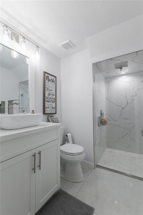 Bathroom featuring a vanity with a white vessel sink, polished chrome faucet, glass-enclosed shower with large-format tile surround, and tile flooring