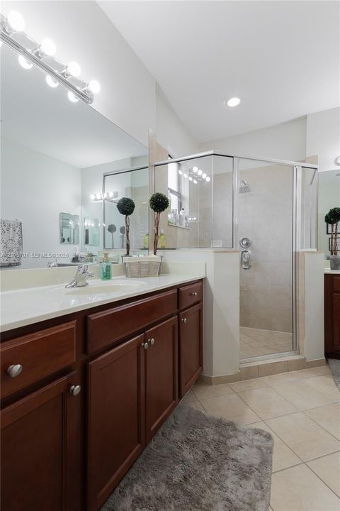 Bathroom featuring dark wood-finish cabinetry, a light-toned countertop with an integrated sink, a full-width vanity mirror, tile flooring, and a glass-enclosed shower with wall-mounted hardware