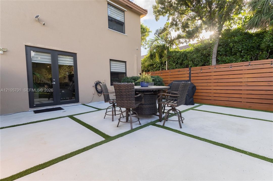 Rear exterior featuring a concrete paver patio with turf inlays, horizontal wood-slat privacy fencing, and double-glass door entry