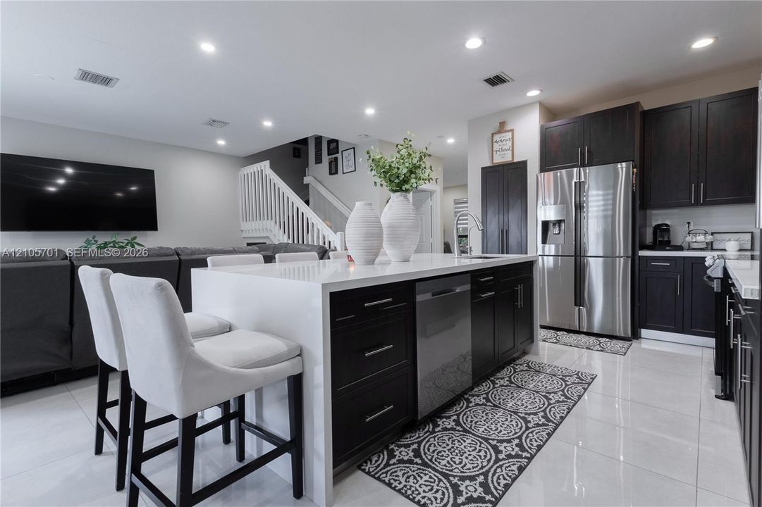 Kitchen featuring a waterfall-edge island with quartz countertop, dark-toned cabinetry, stainless steel appliances, and tile flooring