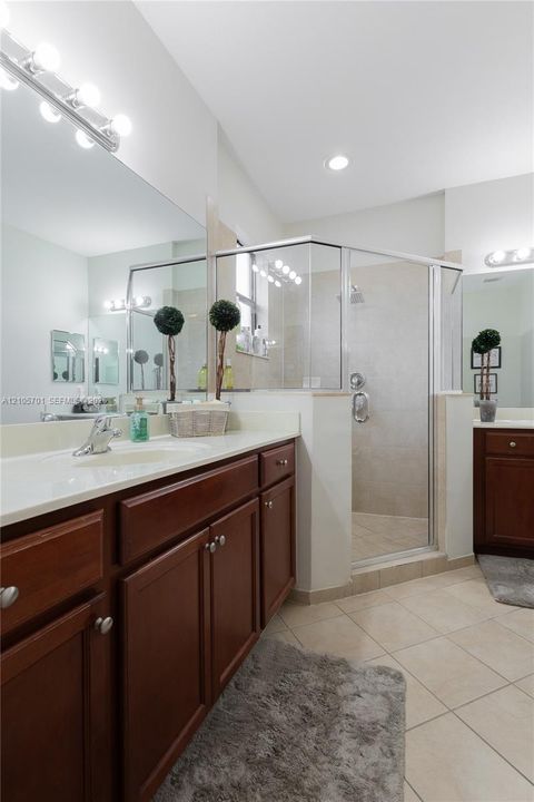 Dual-sink vanity with dark wood cabinetry and solid-surface countertops, large frameless vanity mirrors, and a tiled walk-in shower with glass enclosure