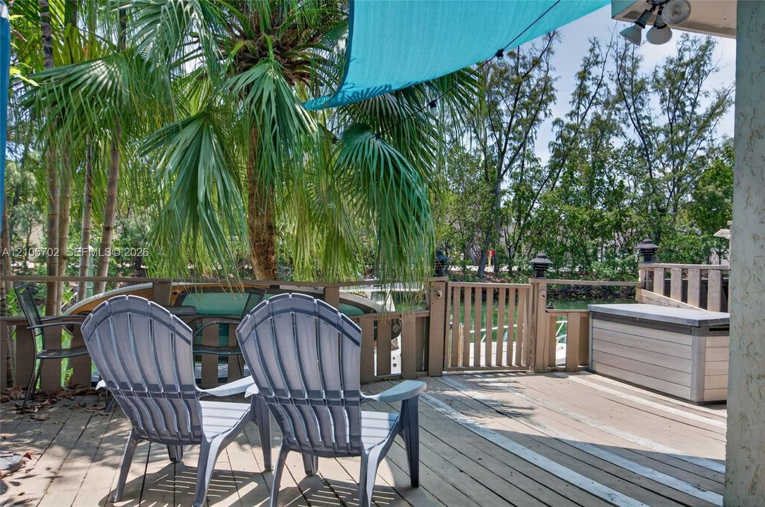 Wood-plank deck featuring a wooden perimeter railing with a gate, mature palm trees, and canal-side positioning