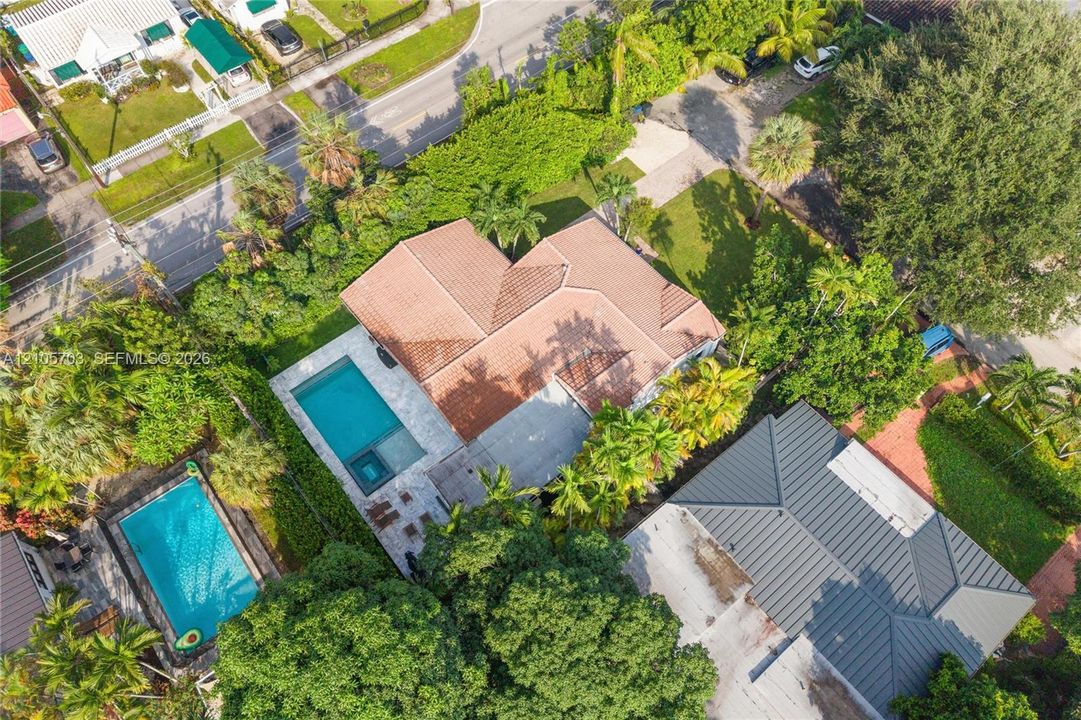 Aerial perspective of property featuring a tile roof, an integrated swimming pool with a spa, and mature landscaping