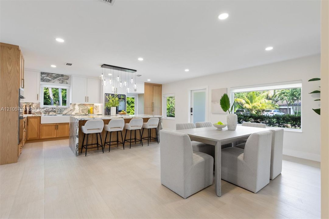 Kitchen featuring wood-finish cabinetry, stone-surface waterfall island with seating, farm-style apron sink, recessed lighting, and large picture windows