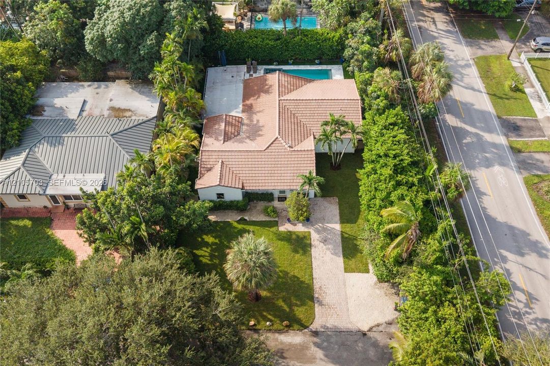 Aerial view featuring a tile roof, an in-ground swimming pool, a concrete patio, and a landscaped yard with mature trees