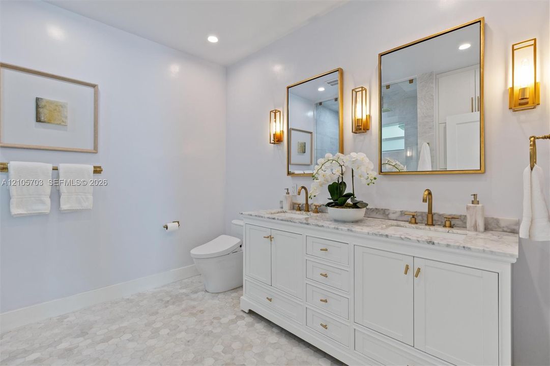 Dual-vanity cabinetry with stone-finish countertops, undermount sinks, brass-toned fixtures, metallic-framed wall mirrors, and wall-mounted sconce lighting