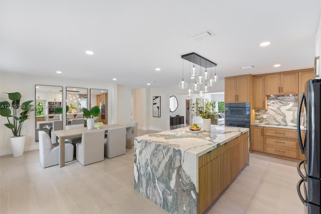 Kitchen featuring a stone-topped waterfall island, custom wood-finish cabinetry, built-in wall oven, recessed lighting, and contemporary multi-pendant light fixture