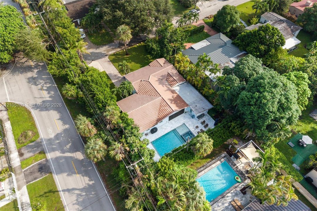 Aerial perspective featuring a tile roof, paved driveway, swimming pool with integrated spa, and mature landscaping