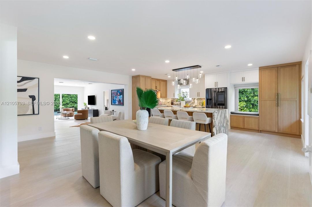 Kitchen and dining area featuring light-tone wood-finish flooring, a waterfall-edge kitchen island, integrated cabinetry, recessed lighting, and a linear multi-pendant light fixture