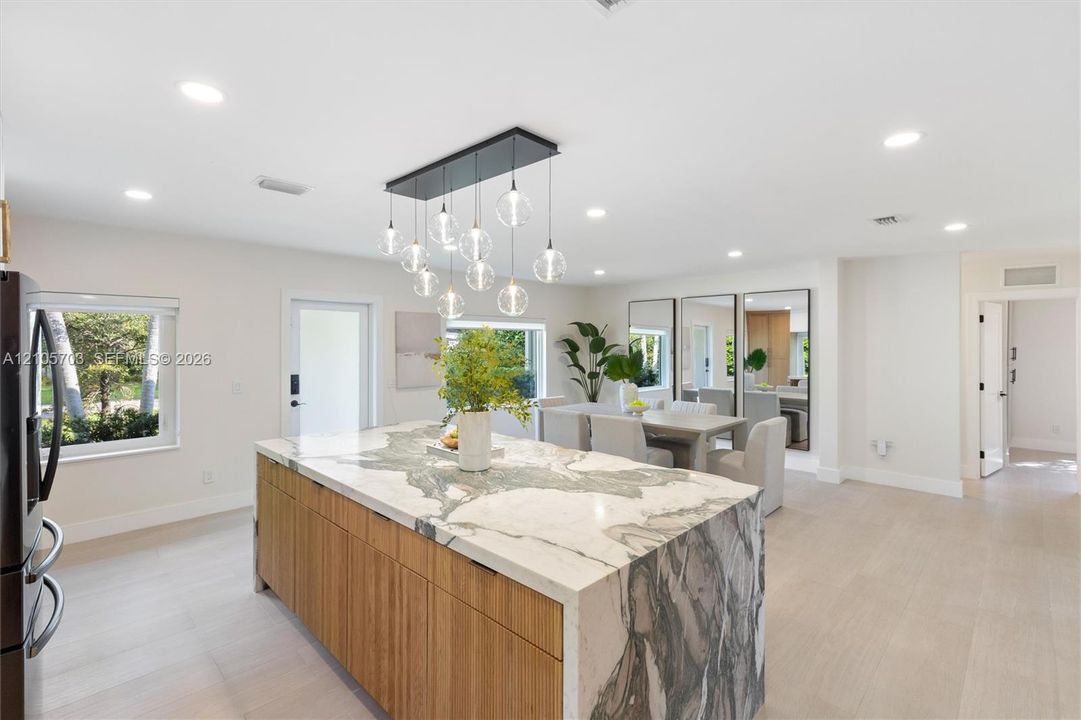 Kitchen island with stone waterfall countertop and natural wood-finish cabinetry, illuminated by a multi-pendant light fixture, complemented by light-toned wood-finish flooring and recessed ceiling lighting